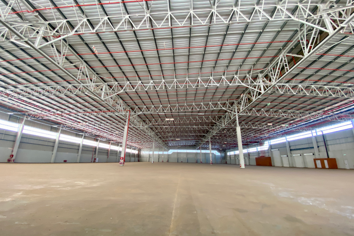 Expansive industrial warehouse space featuring high ceilings with exposed steel trusses, fire sprinkler systems, and polished concrete flooring.