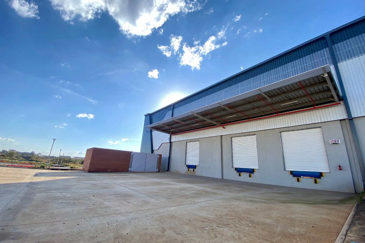 Industrial warehouse exterior featuring multiple loading docks with roller shutter doors, dock levelers, and a large concrete yard area under a protective canopy.