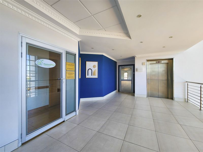 A clean and well-maintained office building hallway featuring tiled flooring, a modern elevator, and professional glass-paneled entrance doors.