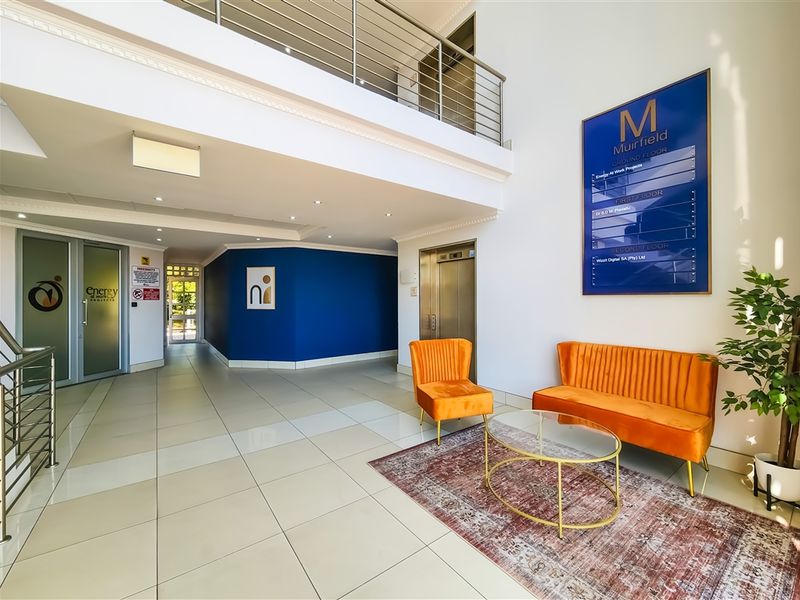 Modern office building entrance lobby featuring a double-volume ceiling, mezzanine level, elevator access, and professional directory signage.