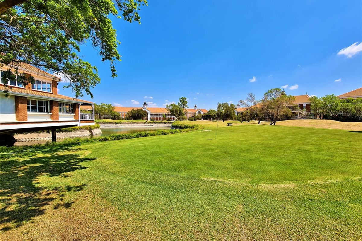 A scenic view of a well-maintained golf course green, water feature, and surrounding office park architecture under a clear blue sky.