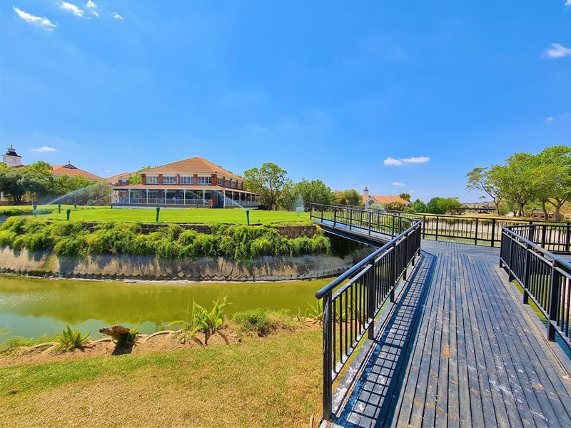 A scenic view of the office property grounds featuring a pedestrian bridge crossing a water feature towards the main building and landscaped lawns.