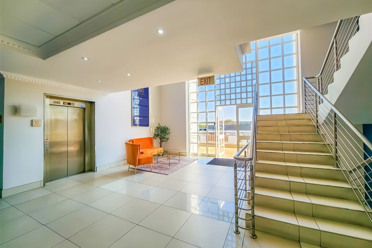 Bright and modern office building lobby featuring polished tile floors, a stainless steel elevator, and a prominent staircase with glass window accents.