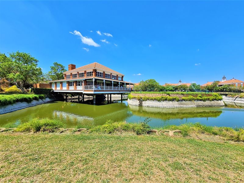 A scenic view of a brick office building elevated over a water feature, featuring a wrap-around balcony and well-maintained landscaping.