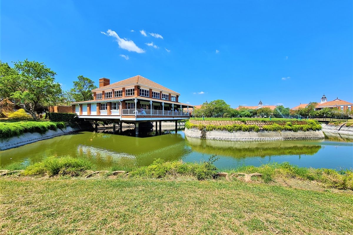 A scenic view of a brick office building elevated over a water feature, featuring a wrap-around balcony and well-maintained landscaping.