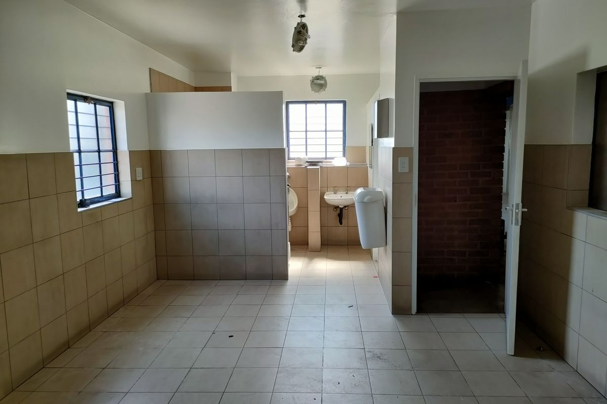 Industrial style bathroom facility featuring tiled walls and floors, a wall-mounted basin, and a separate urinal area with exposed brickwork.