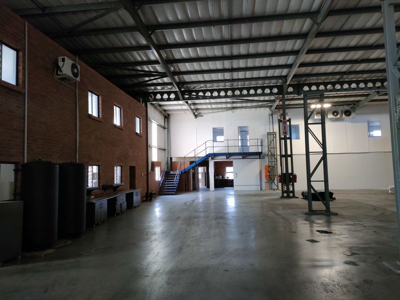 Spacious industrial warehouse featuring high ceilings with exposed steel trusses, polished concrete flooring, a mezzanine level with staircase, and integrated wall-mounted air conditioning units.