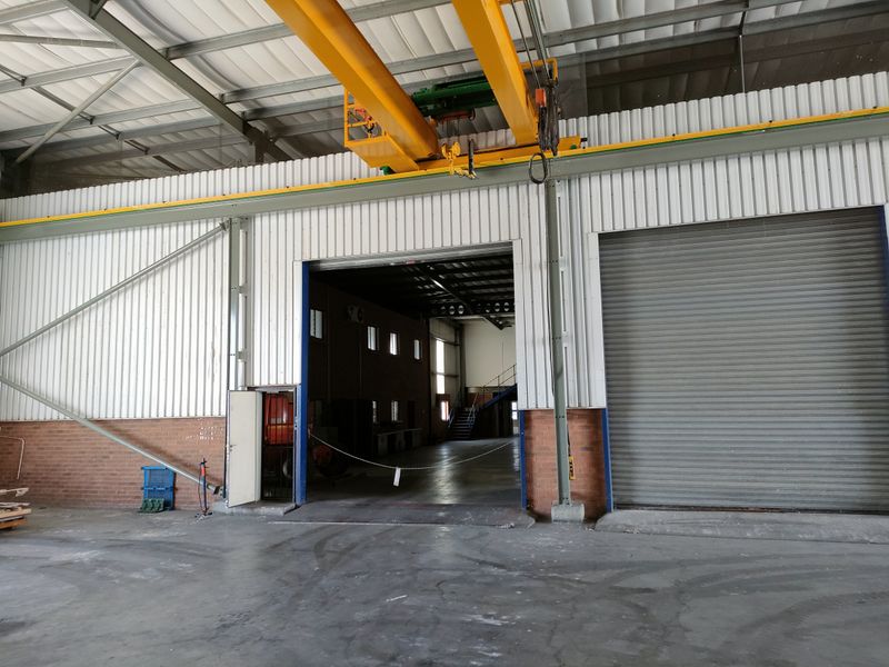 Spacious industrial warehouse area featuring high ceilings, an overhead crane system, and large roller shutter doors for efficient access.