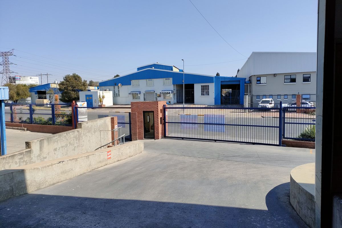 Front view of an industrial property featuring a secure gated entrance, concrete driveway, and warehouse facility with metal cladding.
