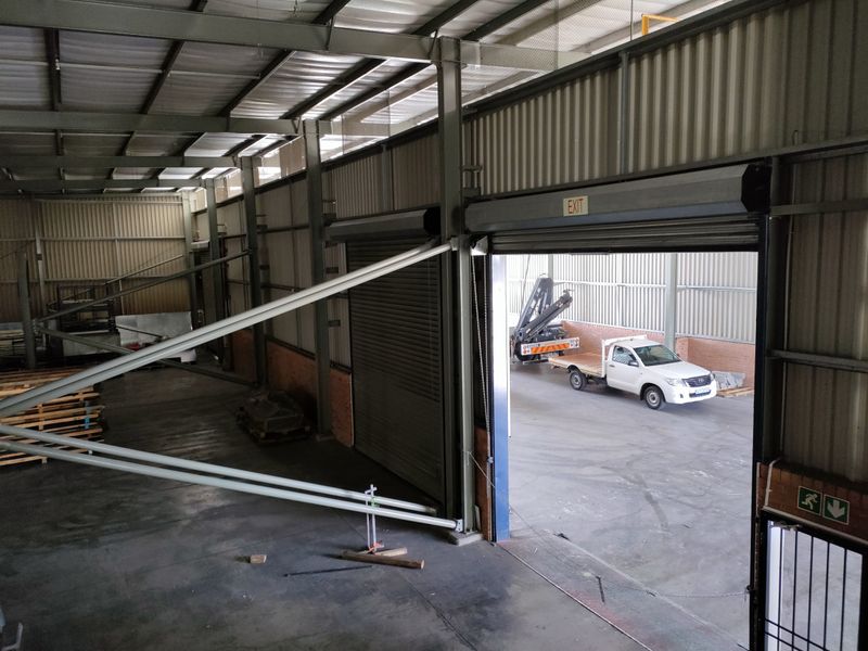 Spacious industrial warehouse unit featuring high ceilings, exposed steel portal frame construction, concrete flooring, and a large roller shutter door for vehicle access.