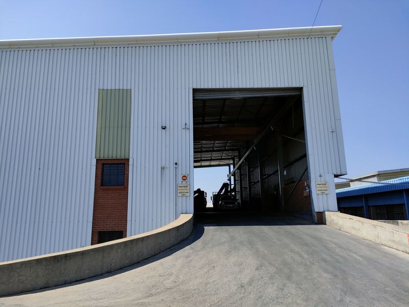 Industrial warehouse exterior featuring a large loading ramp, corrugated metal cladding, and a wide access bay for heavy vehicle entry.