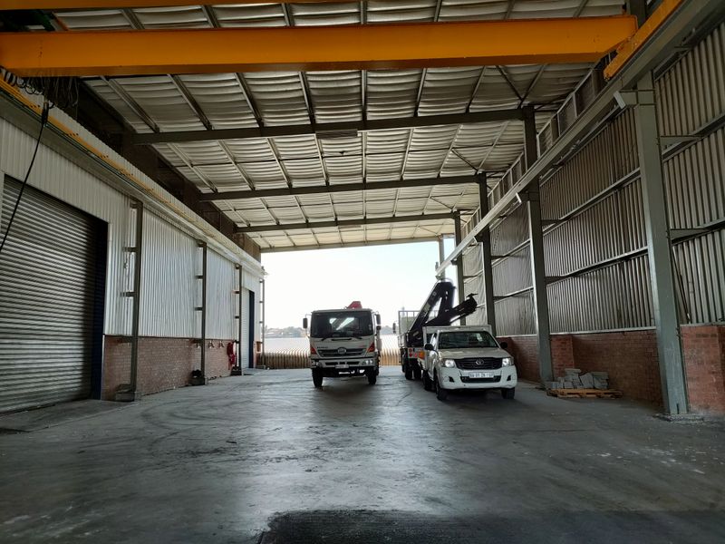 Spacious industrial warehouse featuring high ceilings, an overhead crane system, concrete flooring, and a large roller shutter door for easy vehicle access.