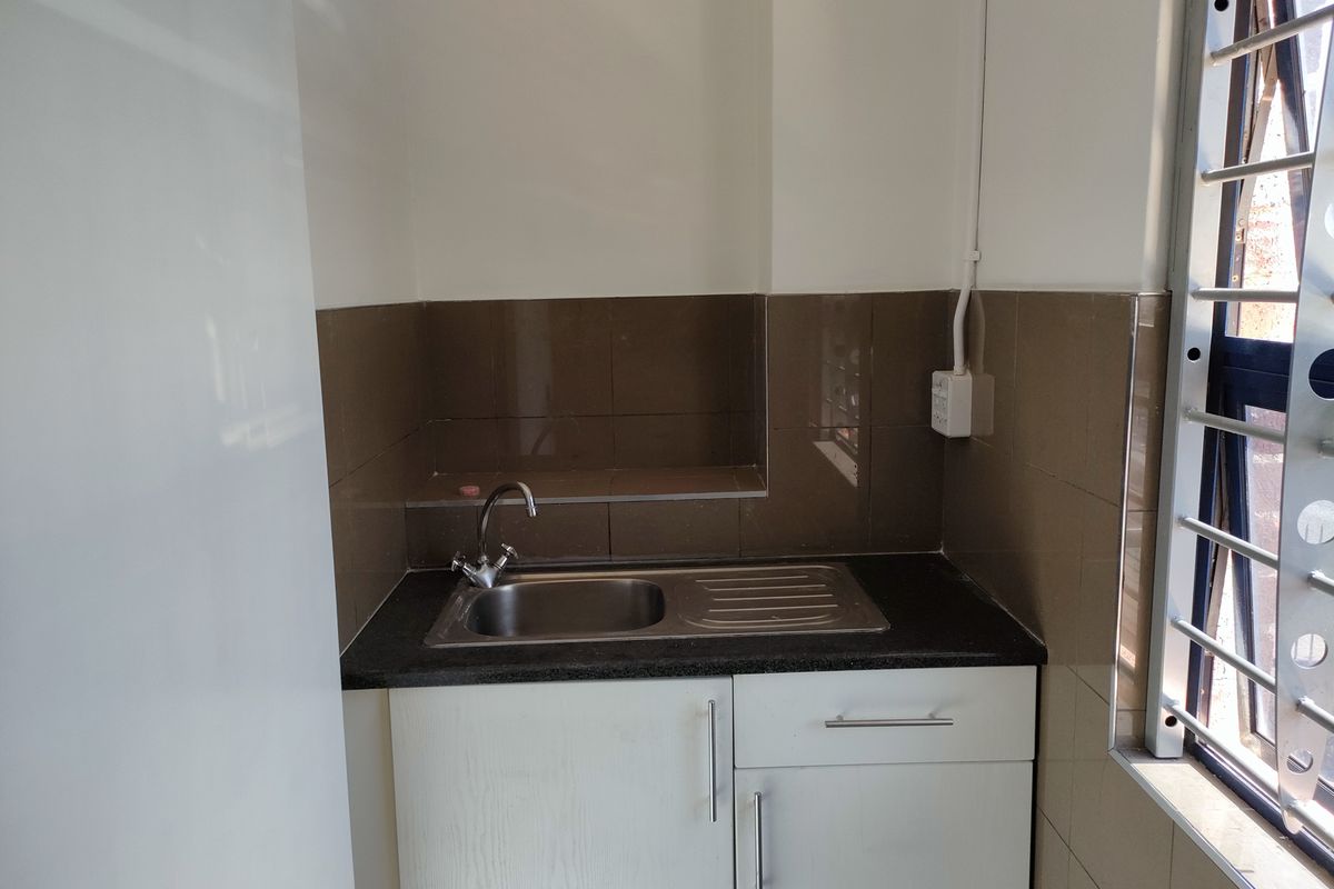 A compact kitchen area featuring a stainless steel sink, built-in white cabinetry, dark laminate countertops, and brown tiled backsplash.