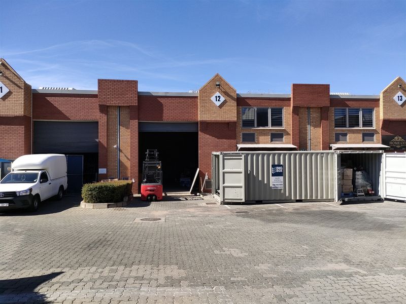 Front elevation of an industrial unit featuring a roller shutter door, brick facade, and paved driveway access.