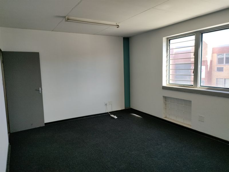 A vacant office space featuring carpet flooring, security bars on the windows, and a fluorescent light fixture, suitable for a professional workspace.