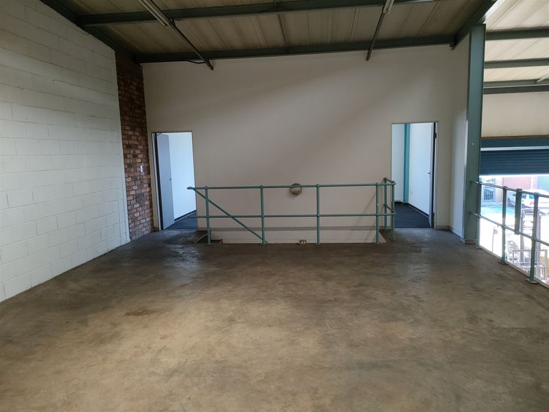 Open-plan industrial mezzanine level featuring concrete flooring, exposed brickwork, and metal safety railings, suitable for storage or office conversion.