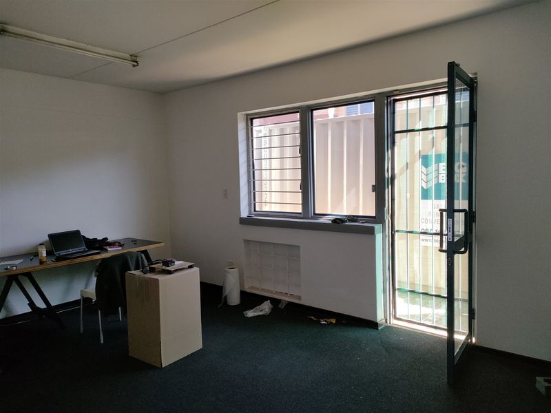 A functional office space featuring security bars on windows, a security gate, and carpet flooring, suitable for industrial or commercial use.