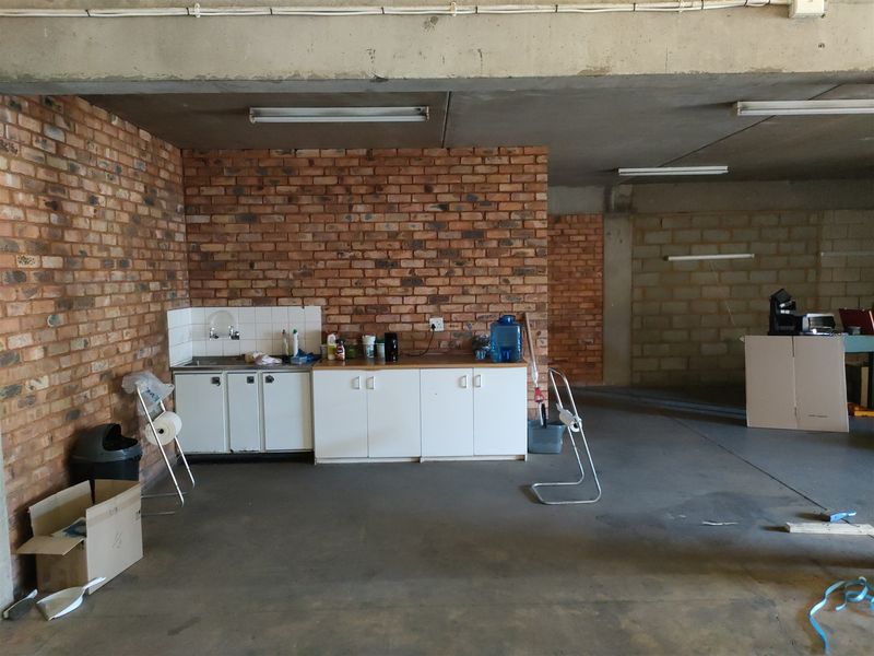 Industrial utility space featuring exposed brick walls, concrete flooring, and a basic kitchenette area with built-in cabinetry and a sink.