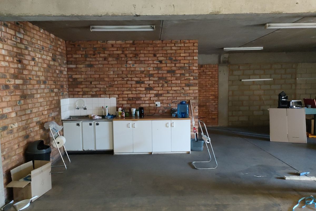 Industrial utility space featuring exposed brick walls, concrete flooring, and a basic kitchenette area with built-in cabinetry and a sink.
