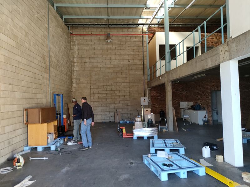 Spacious industrial warehouse unit featuring high ceilings, exposed brickwork, a mezzanine level with metal railing, and durable concrete flooring.