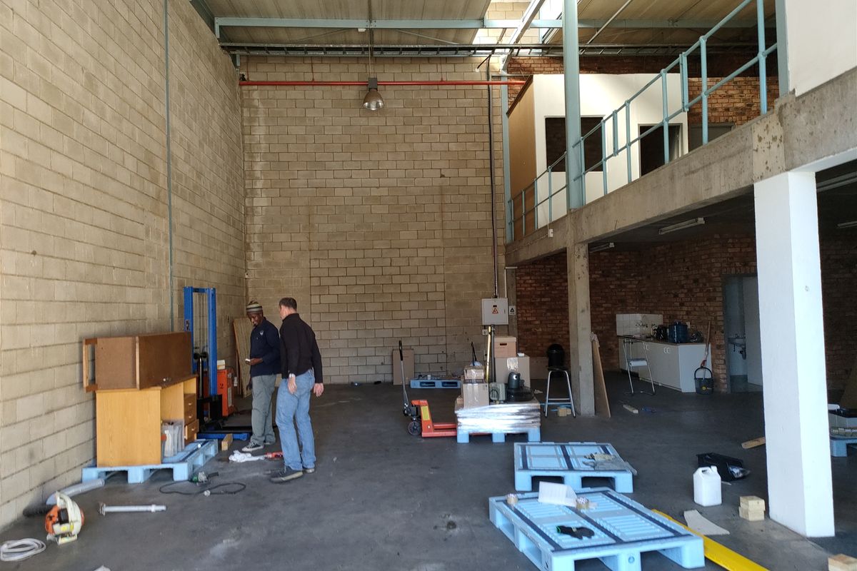 Spacious industrial warehouse unit featuring high ceilings, exposed brickwork, a mezzanine level with metal railing, and durable concrete flooring.