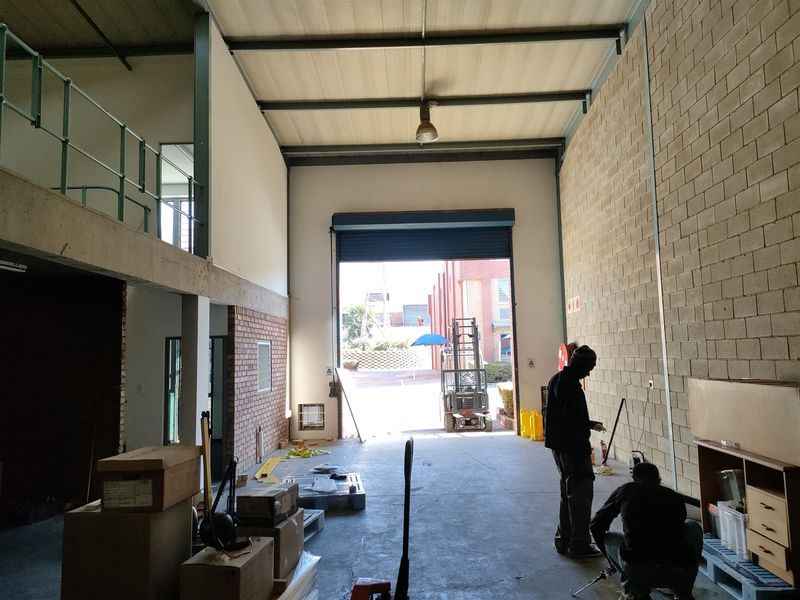 Spacious industrial warehouse unit featuring a high-clearance roller shutter door, mezzanine level, and exposed brick walls, suitable for various commercial or storage operations.