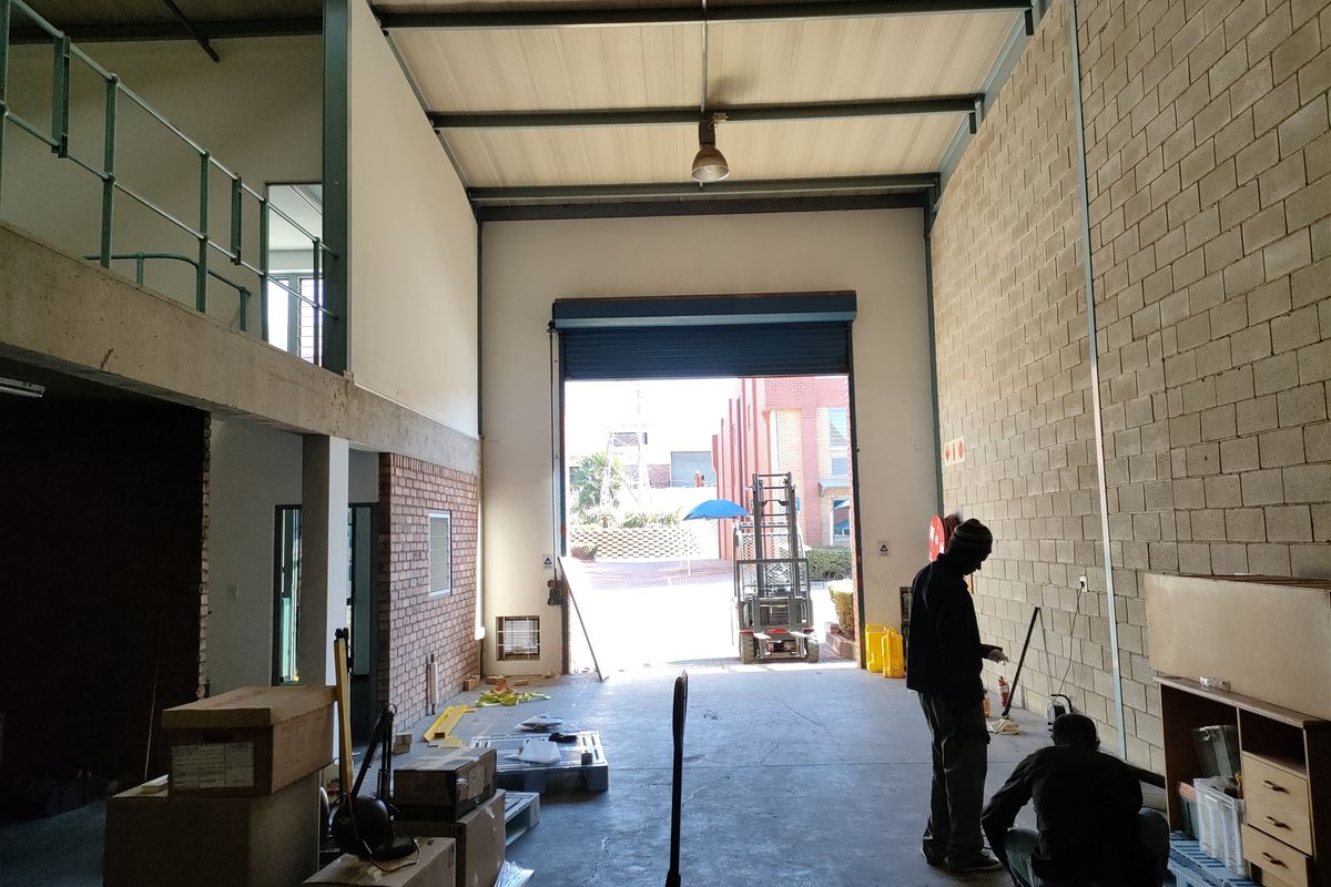 Spacious industrial warehouse unit featuring a high-clearance roller shutter door, mezzanine level, and exposed brick walls, suitable for various commercial or storage operations.