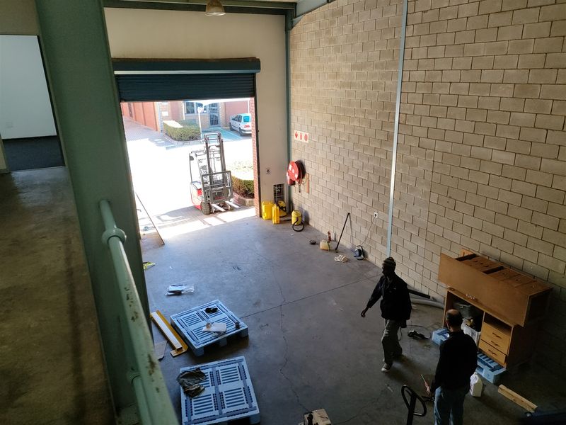 Industrial warehouse space featuring high ceilings, exposed concrete block walls, concrete flooring, and a large roller shutter door for vehicle access.