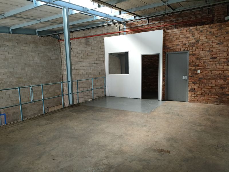 Spacious industrial utility area featuring exposed brickwork, steel roof trusses, concrete flooring, and a partitioned internal office space.