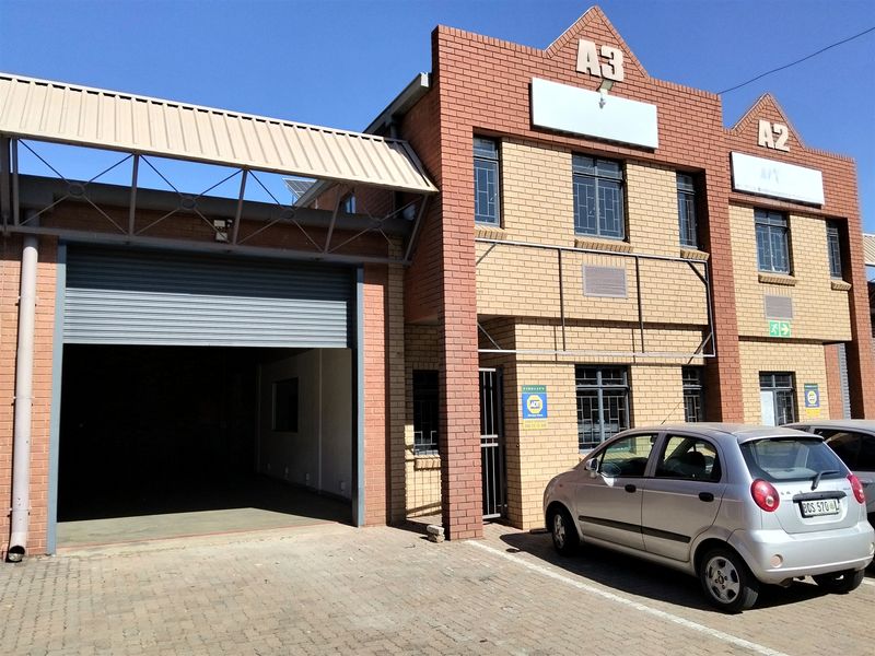 Front elevation of an industrial unit featuring a large roller shutter door, brick facade, and paved parking area.