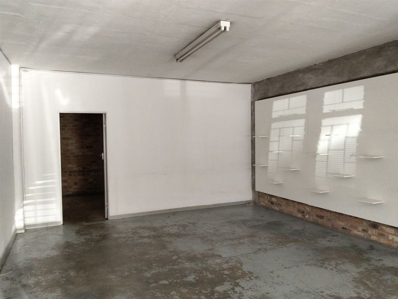 An open-plan utility or storage space featuring industrial concrete flooring, exposed brick accents, and a wall-mounted shelving unit.