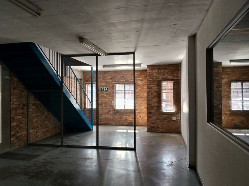 Industrial style utility space featuring exposed brick walls, concrete flooring, a metal staircase, and a glass partition, offering a versatile open-plan layout.