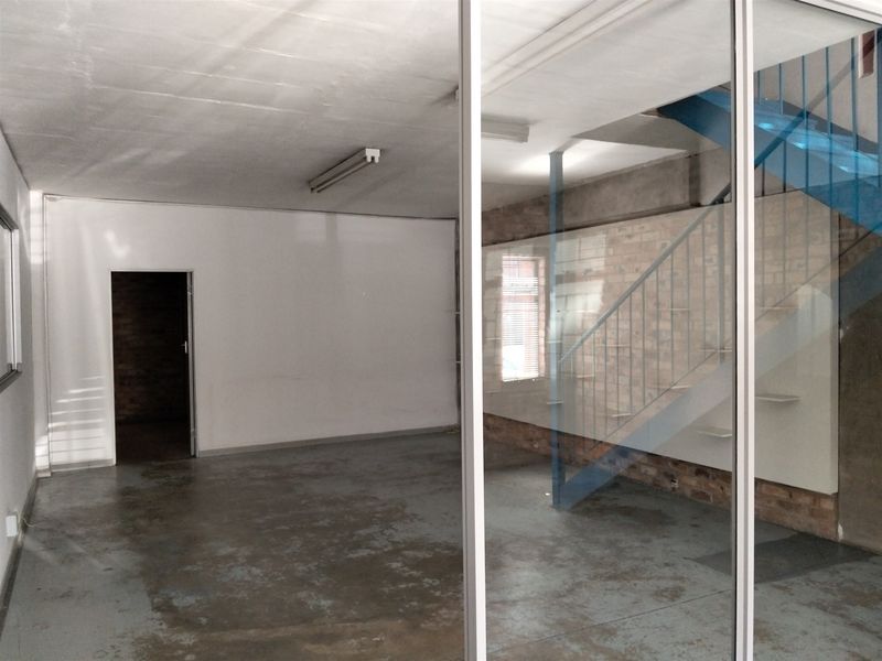 Open-plan industrial space featuring exposed brick walls, concrete flooring, and a metal staircase, offering a versatile layout for various commercial or creative uses.