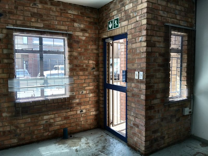 Industrial style entry area featuring exposed brick walls, concrete flooring, and a secure metal entrance door with an emergency exit sign.