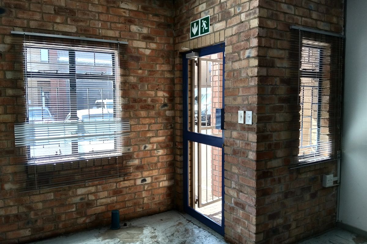 Industrial style entry area featuring exposed brick walls, concrete flooring, and a secure metal entrance door with an emergency exit sign.
