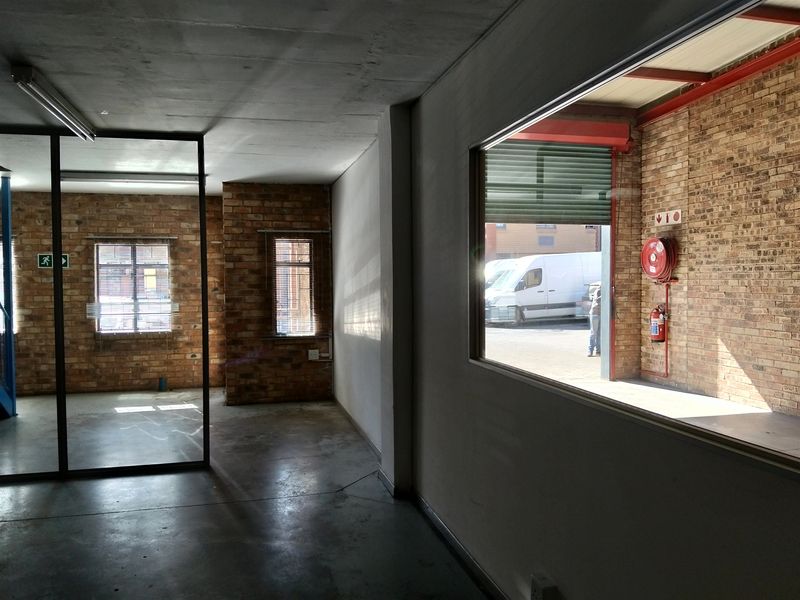 Empty industrial office space featuring exposed brick walls, concrete flooring, and a large glass partition overlooking the warehouse area.