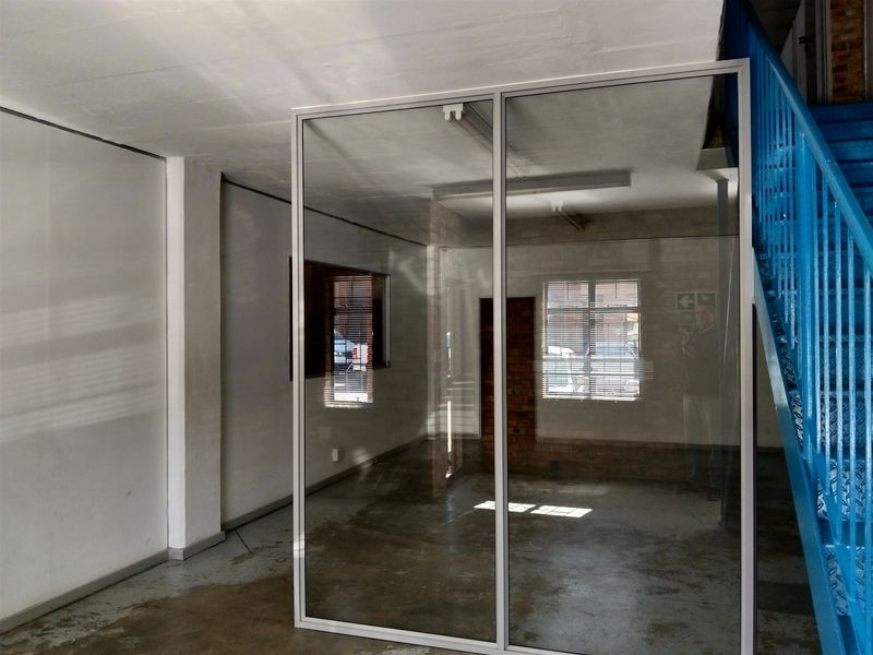 Open-plan industrial office space featuring a glass partition, exposed brick accents, and a prominent blue metal staircase.
