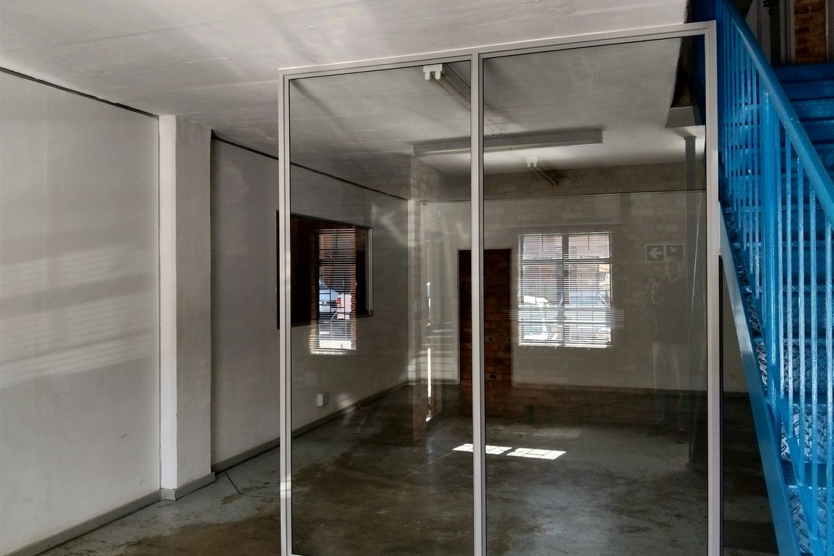 Open-plan industrial office space featuring a glass partition, exposed brick accents, and a prominent blue metal staircase.