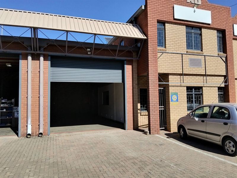 Front elevation of an industrial unit featuring a large roller shutter door, brick facade, and paved driveway access.