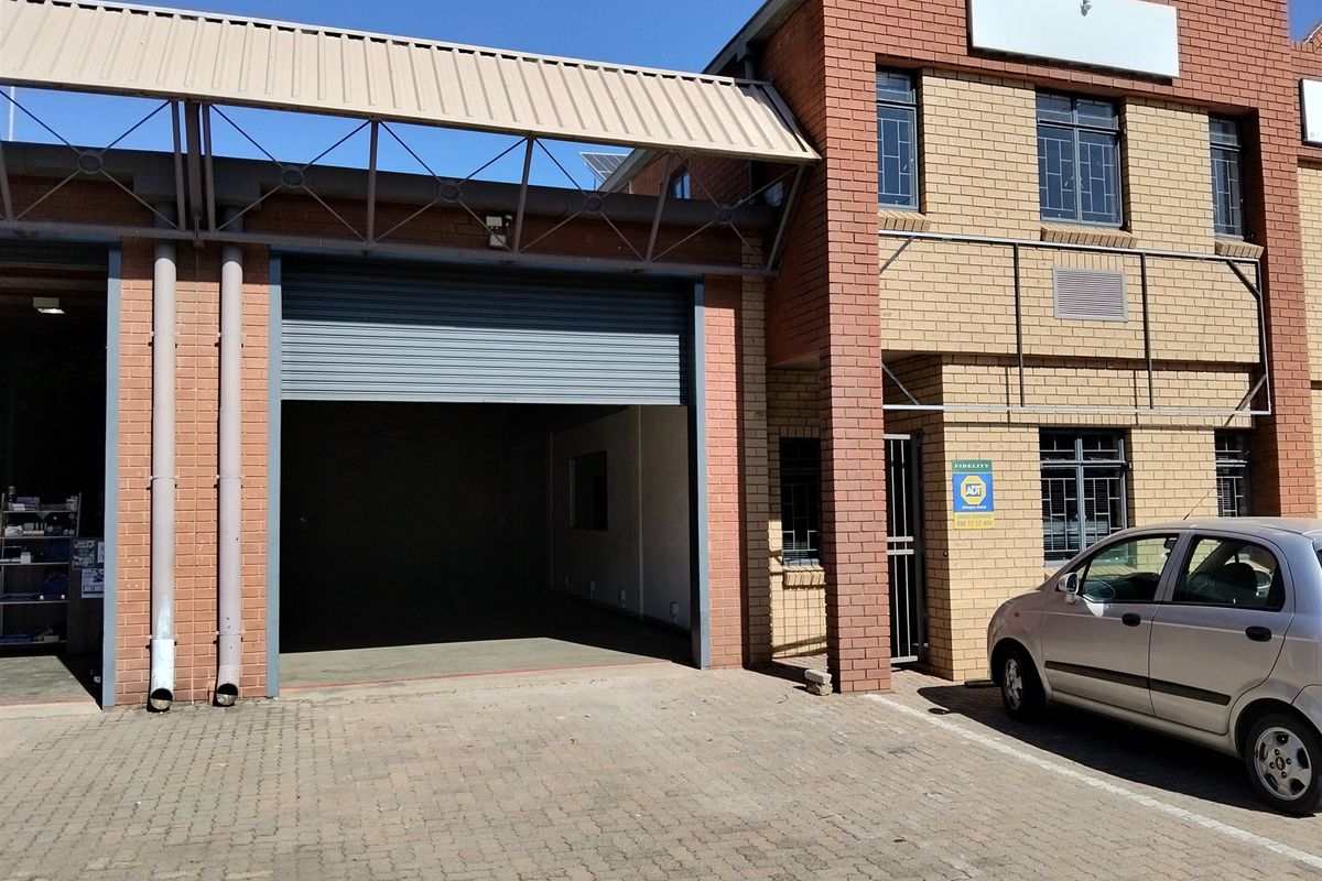 Front elevation of an industrial unit featuring a large roller shutter door, brick facade, and paved driveway access.