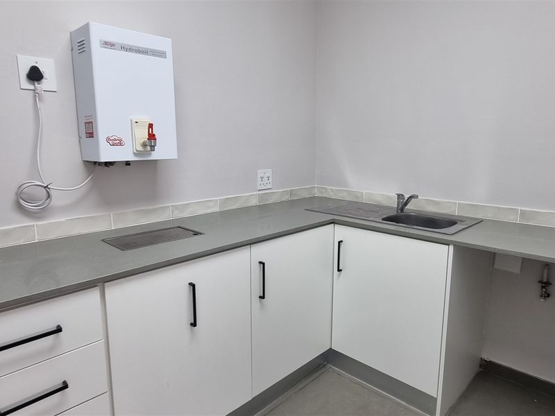 A clean, modern kitchenette featuring white cabinetry, stone countertops, a stainless steel sink, and a wall-mounted boiling water dispenser.