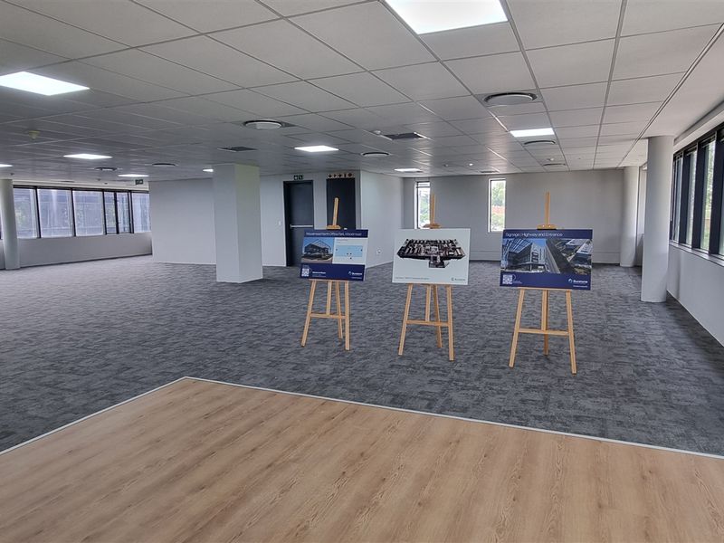 A spacious, open-plan office area featuring modern carpet tiles, laminate flooring, recessed lighting, and extensive windows providing ample natural light.