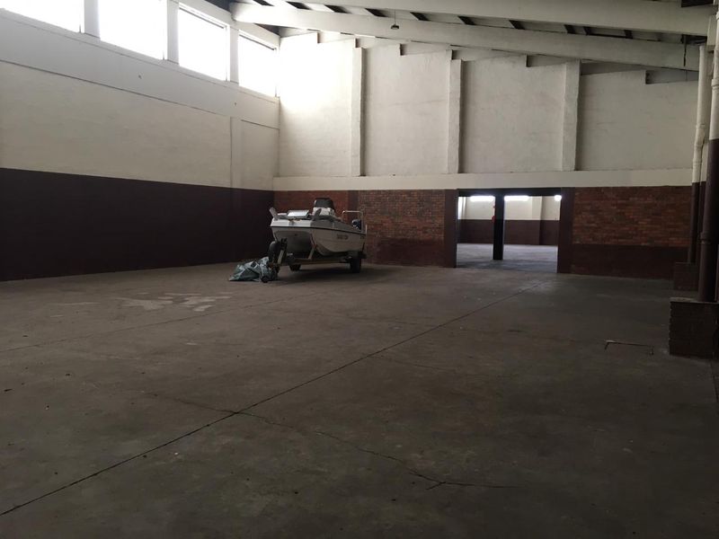 Spacious industrial utility area featuring high ceilings, exposed brickwork, and durable concrete flooring, suitable for storage or workshop use.
