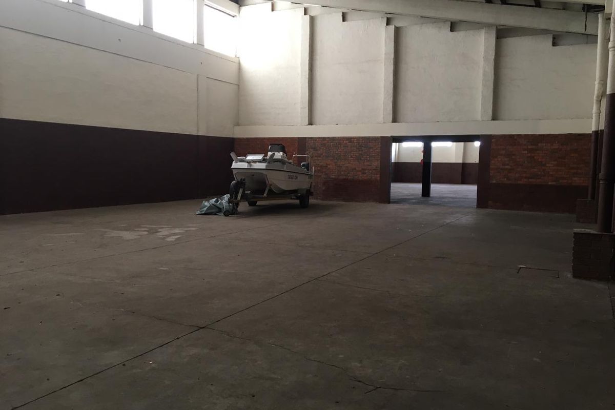 Spacious industrial utility area featuring high ceilings, exposed brickwork, and durable concrete flooring, suitable for storage or workshop use.