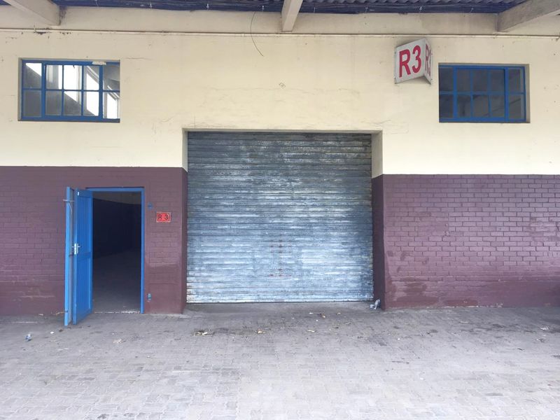 Industrial unit exterior featuring a large roller shutter door, separate pedestrian access, and paved forecourt area.