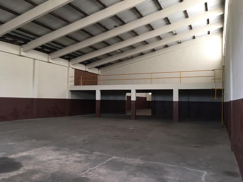 Spacious industrial warehouse unit featuring high ceilings with exposed steel trusses, a mezzanine level with safety railing, and durable concrete flooring.