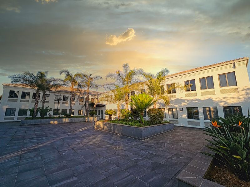 A well-maintained office building exterior featuring a paved courtyard, landscaped garden beds, and a professional multi-story facade at sunset.