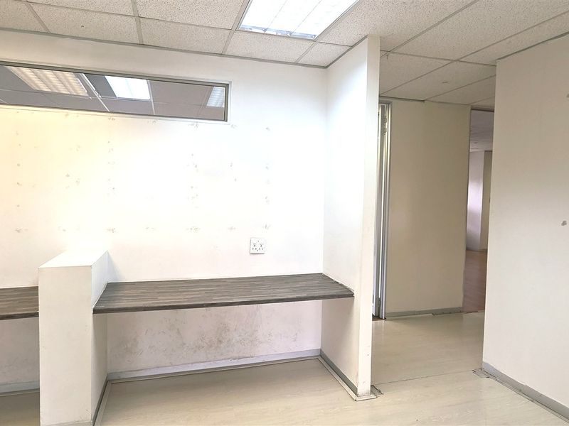 An empty office space featuring a built-in desk, suspended ceiling with recessed lighting, and a clere-story window, requiring minor cosmetic wall repairs.