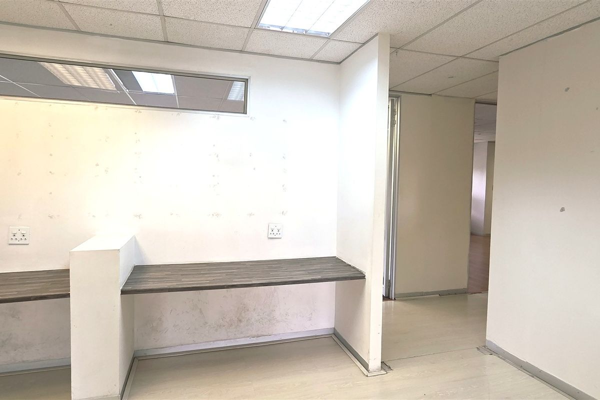 An empty office space featuring a built-in desk, suspended ceiling with recessed lighting, and a clere-story window, requiring minor cosmetic wall repairs.