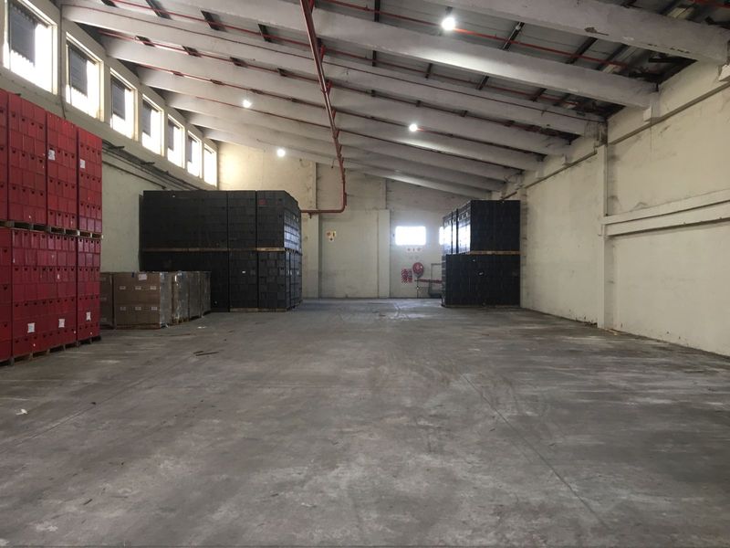 Spacious industrial warehouse featuring high ceilings with exposed trusses, concrete flooring, fire sprinkler system, and natural light from high-level windows.